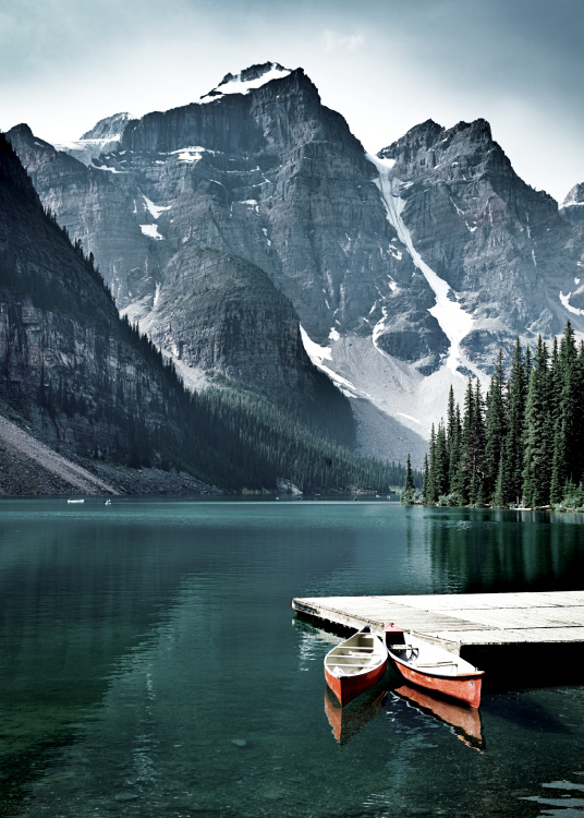  – Fotografi av en innsjø med en liten brygge og to kanoer foran fjell