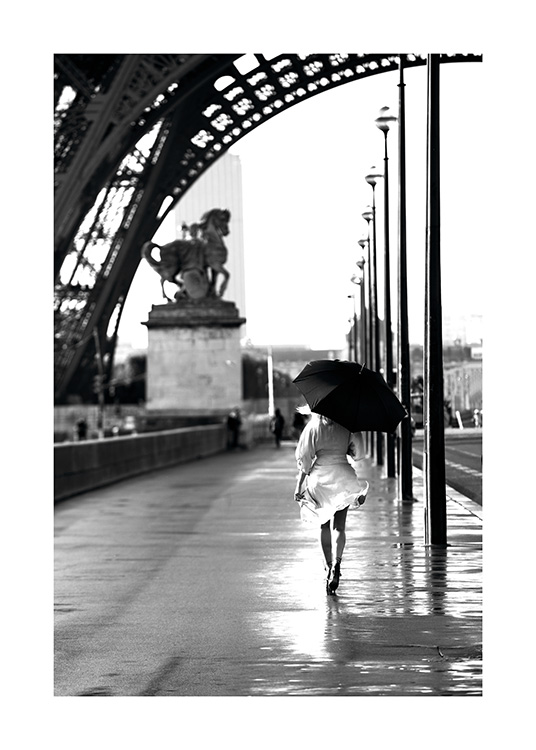  – Svarthvitt-fotografi av en kvinne som går med en paraply under Eiffeltårnet