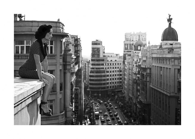 Svarthvitt-fotografi av en kvinne som ser ned på byen fra et tak