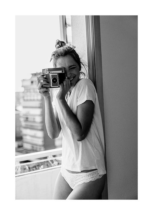 Svarthvitt-fotografi av en kvinne som smiler mens hun holder et kamera og er iført en hvit t-skjorte