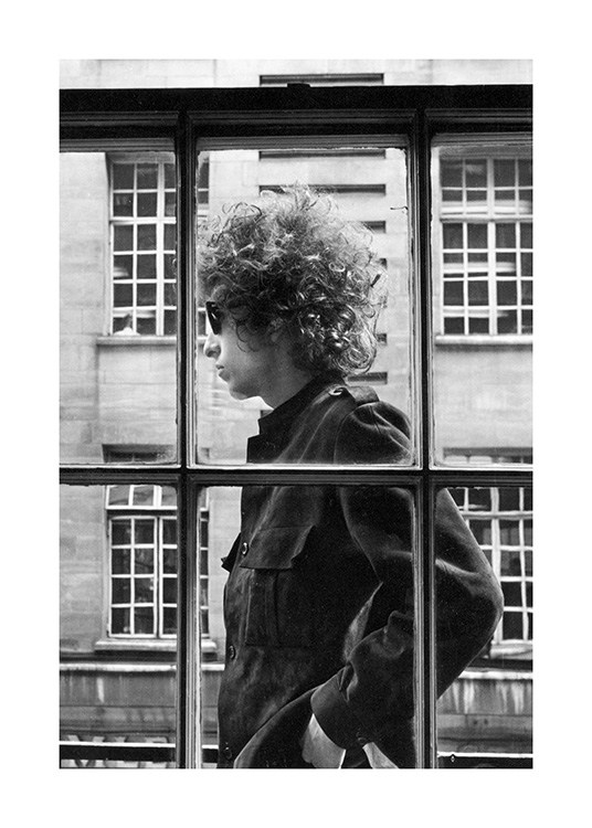  - Svarthvitt-fotografi av Bob Dylan som står utenfor et vindu