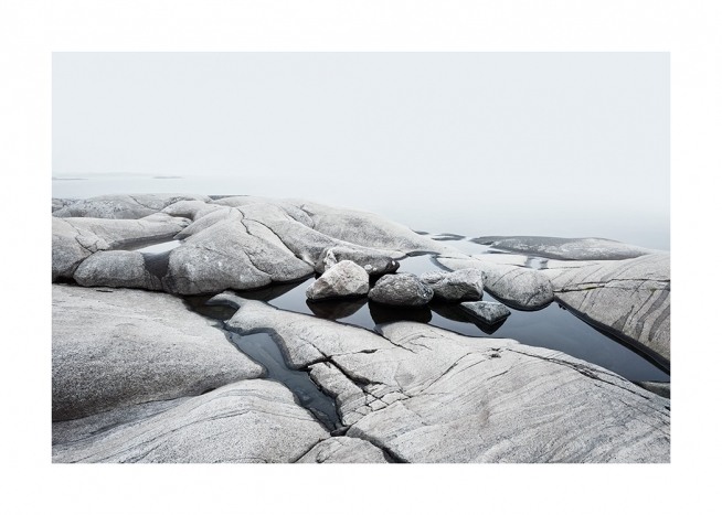  – Fotografi av en kystlinje med glatte steiner med vann mellom