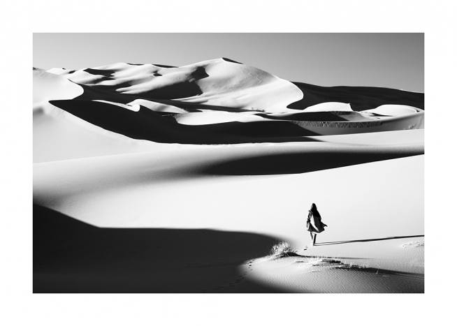  – Svarthvitt-fotografi av en ørken, med en kvinne som går mellom sanddynene