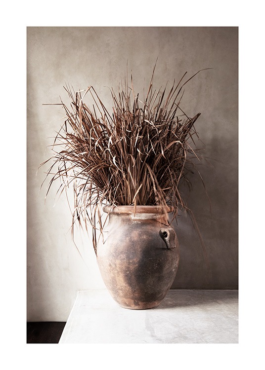  – Fotografi av tørket, beige gress i en vase mot en beige betongvegg