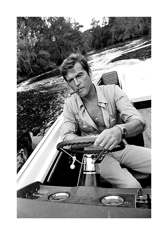  – Svarthvitt-fotografi av Roger Moore som kjører båt med en sigarett i munnen