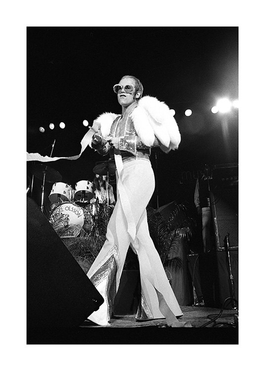  – Svarthvitt-fotografi av sangeren Elton John iført en hvit jumpsuite og solbriller på scenen