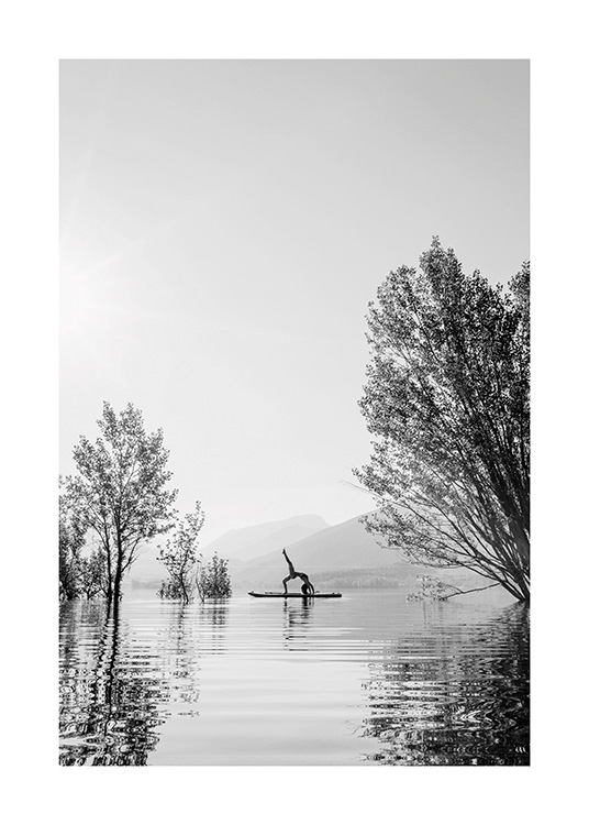  – Svarthvitt-fotografi av en kvinne i en yogaposisjon på et surfebrett midt i en innsjø