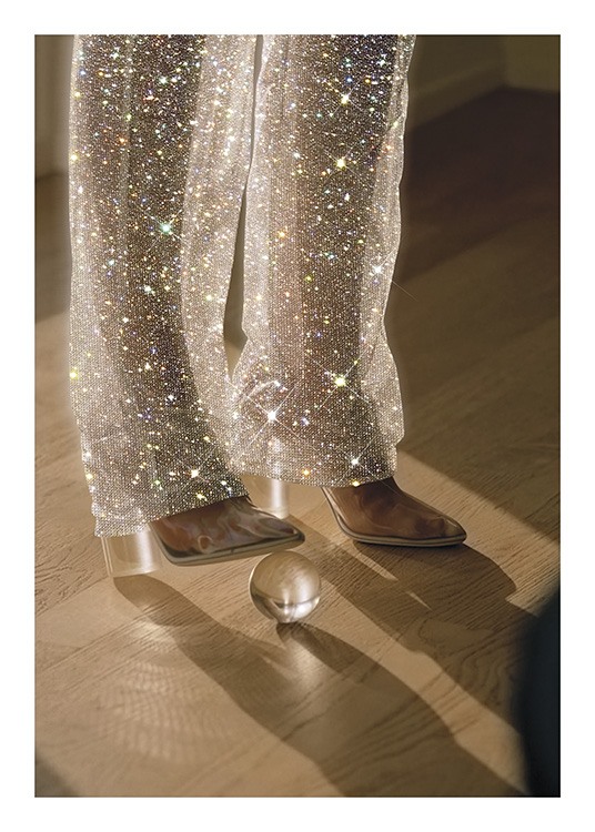  – Fotografi av en kvinne med en glasskule under hælen, iført glitrende bukser