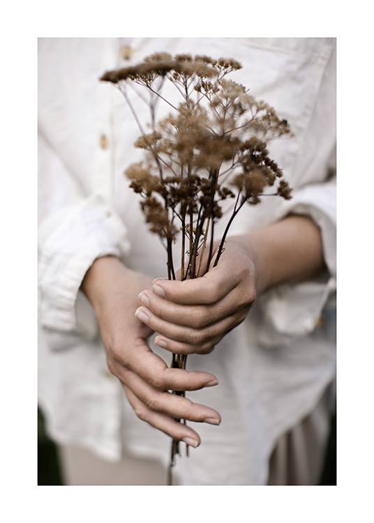  – Fotografi av en kvinne som holder en bukett tørkede blomster, med hvit linskjorte i bakgrunnen