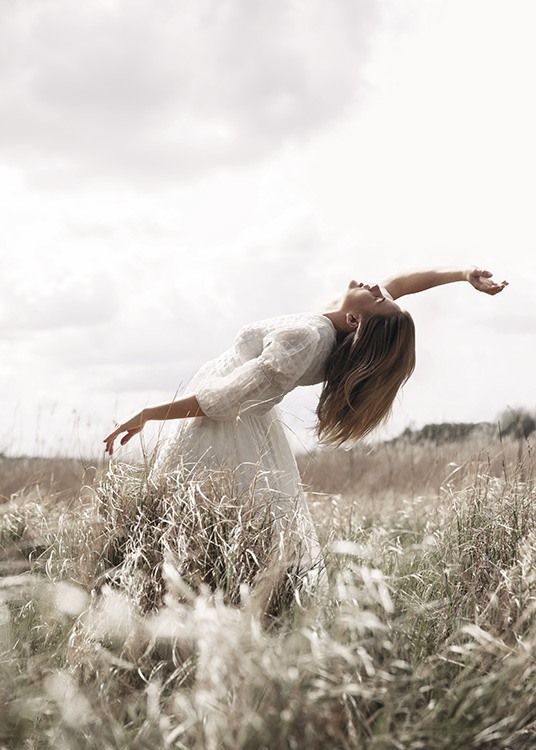  – Fotografi av en kvinne som poserer i en eng med gress, iført en hvit kjole