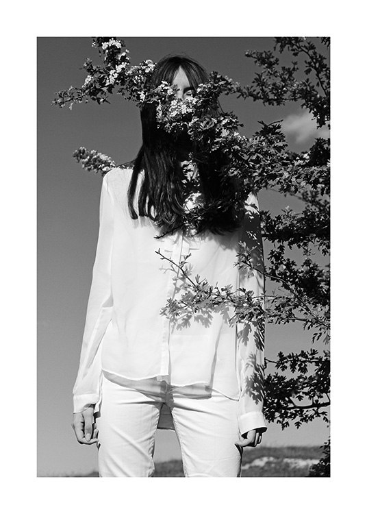  – Svarthvitt-fotografi av en kvinne i hvite klær, med en tregrein foran seg