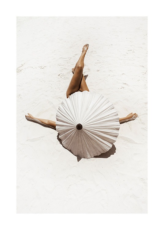  – Fotografi av en kvinne som ligger på hvit sand med beina i kryss, dekket av en beige parasoll