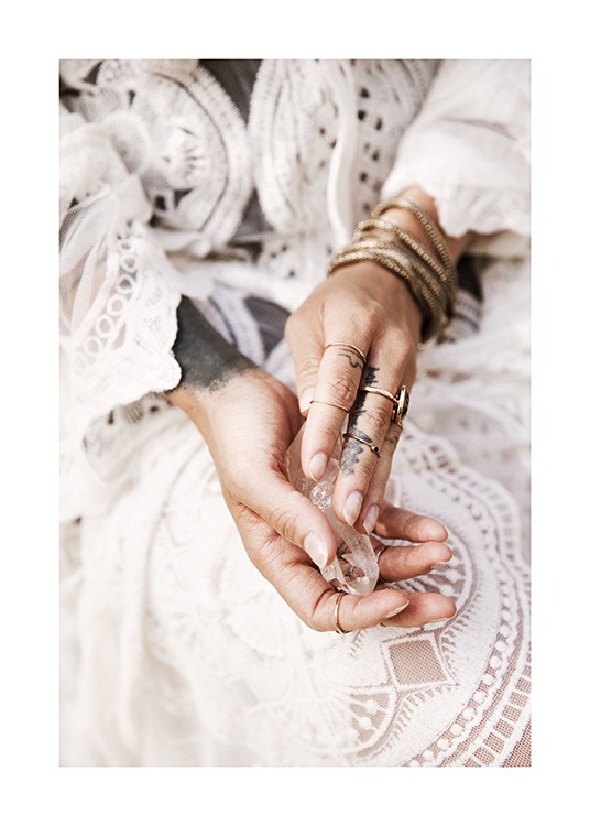  – Fotografi av hender som holder en krystall, med gullsmykker og en hvit blondekjole i bakgrunnen