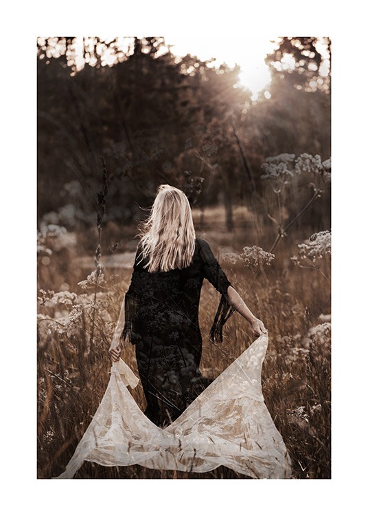  – Fotografi av en kvinne som går i en åker iført en svart kjole mens hun holder hvite blonder bak seg
