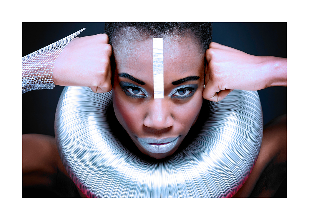  – Fotografi av en kvinne med knyttnevene mot tinningen og et stort, sølvfarget rør rundt halsen