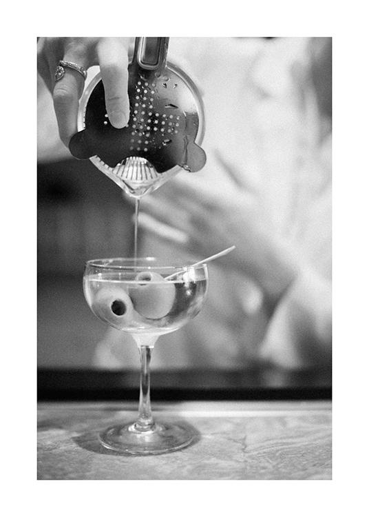  – Svarthvitt-fotografi av en martini som helles fra en shaker, med oliven i glasset