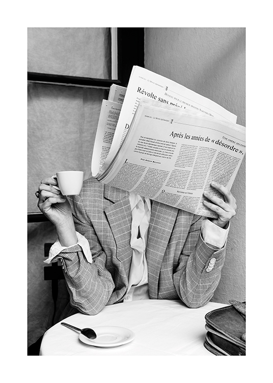  – Svarthvitt-fotografi av en person som sitter ved et kafébord med en avis foran ansiktet