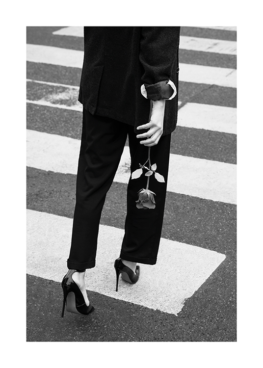  – Svarthvitt-fotografi av en kvinne som går over en fotgjengerovergang, iført dress og høyhælte sko og med en rose i hånden