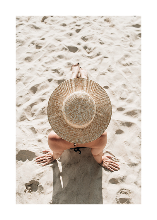  – Fotografi av en kvinne som sitter i sanden, iført en solhatt, tatt ovenfra