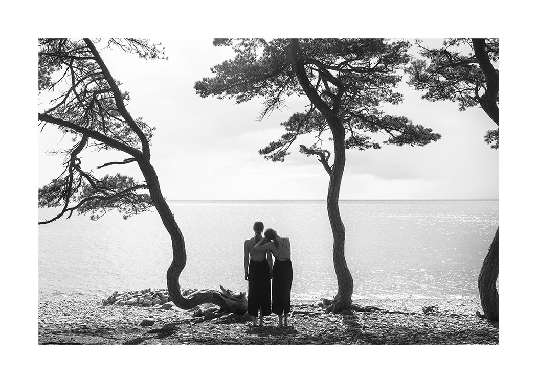  – Svarthvitt-fotografi av to kvinner som ser ut over vannet fra en strand med trær