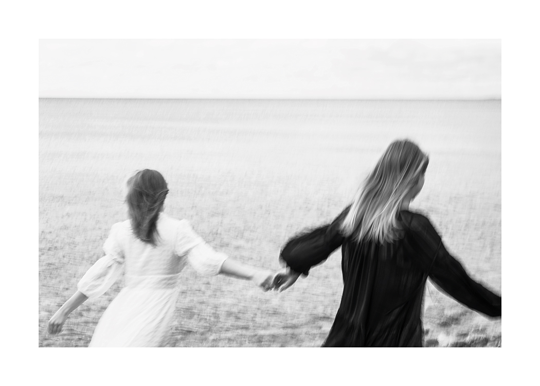  – Svarthvitt-fotografi av to kvinner som løper over en eng mens de holder hverandre i hendene