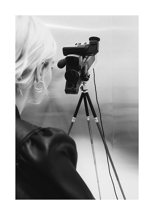  – Svarthvitt-fotografi av en kvinne med blondt hår som står bak et videokamera