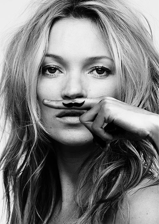  – Svarthvitt-fotografi av Kate Moss med en finger over munnen med en bart på fingeren
